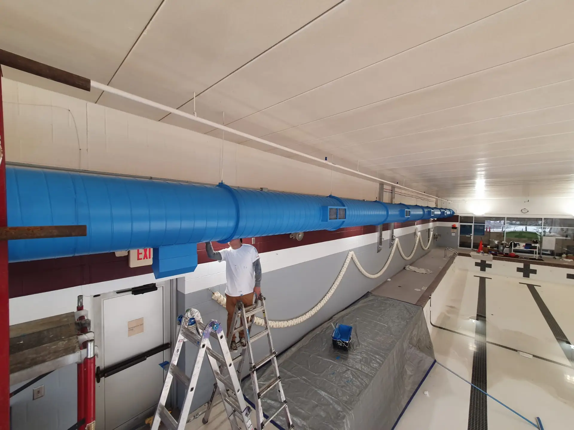 a man on a ladder on a ladder in a room with a large blue tube